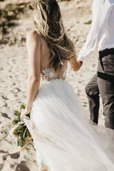 Rückansicht von Braut und Bräutigam beim Spaziergang am Strand - LHPF00796
