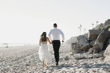 Rear view of bride and groom running on the beach - LHPF00804