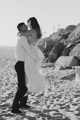 Glückliche Braut und Bräutigam umarmen sich am Strand - LHPF00806