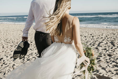 Rear view of bride and groom walking on the beach - LHPF00809