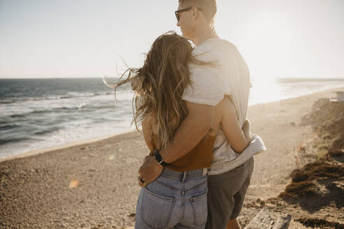Verliebtes junges Paar genießt die Aussicht auf den Strand bei Sonnenuntergang - LHPF00820