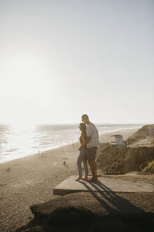 Verliebtes junges Paar genießt die Aussicht auf den Strand bei Sonnenuntergang - LHPF00821
