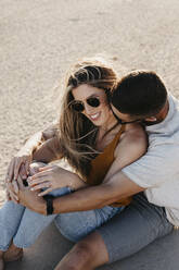 Happy affectionate young couple sitting on the beach - LHPF00823