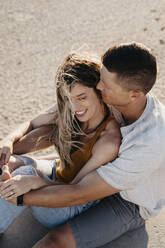 Happy affectionate young couple sitting on the beach - LHPF00824