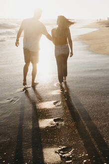 Verliebtes junges Paar, das bei Sonnenuntergang am Meer spazieren geht - LHPF00836
