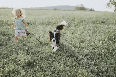 Mädchen läuft mit Hund auf einer Wiese auf dem Lande - DWF00492