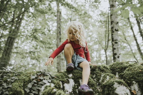 Blond girl sitting on rock in the forest - DWF00494