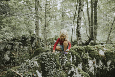 Blond girl sitting on rock in the forest - DWF00495