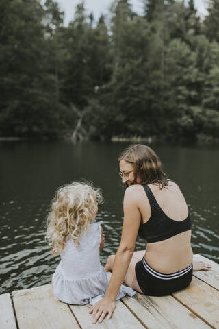 Mutter und Tochter sitzen auf einem Steg an einem See, lizenzfreies Stockfoto