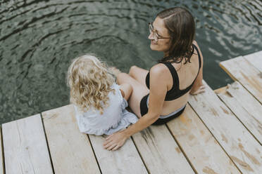 Mother and daughter sitting on jetty at a lake - DWF00499