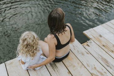 Mother and daughter sitting on jetty at a lake - DWF00500