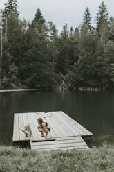 Mother and daughter crouching on jetty at a lake - DWF00501