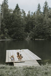 Mutter und Tochter kauernd auf einem Steg am See - DWF00501