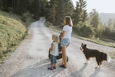 Mother with daughter, stroller and dog standing on forest path - DWF00507