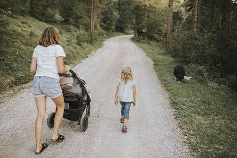 Mutter mit Tochter, Kinderwagen und Hund auf einem Waldweg, lizenzfreies Stockfoto