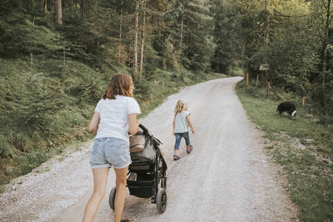 Mother with daughter, stroller and dog walking on forest path stock photo