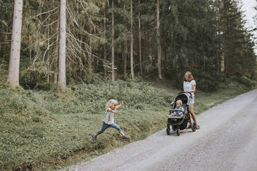 Mother with daughter and baby in stroller in forest - DWF00511