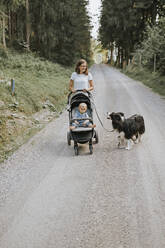 Mutter mit Baby im Kinderwagen und Hund beim Spaziergang auf einem Waldweg - DWF00512