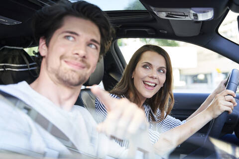 Glückliches Paar in einem Auto mit Frau am Steuer und Mann, der mit dem Finger zeigt, lizenzfreies Stockfoto