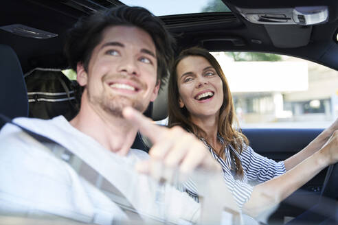 Glückliches Paar in einem Auto mit Frau am Steuer und Mann, der mit dem Finger zeigt - PNEF01978
