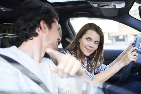 Glückliches Paar in einem Auto mit Frau am Steuer und Mann, der mit dem Finger zeigt - PNEF01979