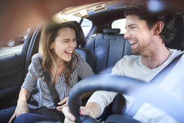 Laughing couple in a car with man driving - PNEF01989