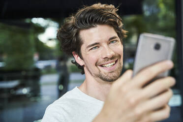 Porträt eines glücklichen Mannes mit Handy in der Hand in der Stadt - PNEF02029