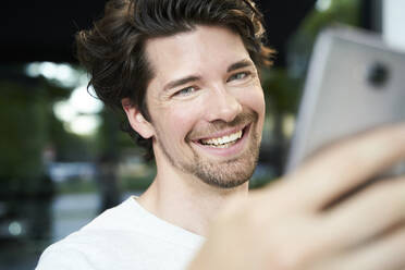Porträt eines glücklichen Mannes mit Handy in der Hand in der Stadt - PNEF02030