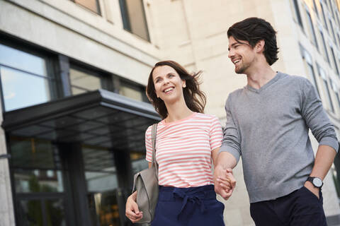 Glückliches Paar beim Spaziergang Hand in Hand in der Stadt, lizenzfreies Stockfoto