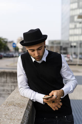 Young man dressed in black and white leaning on wall looking at cell phone stock photo