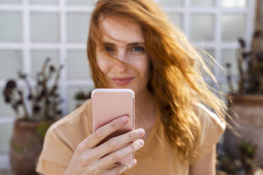 Hand einer lächelnden rothaarigen jungen Frau, die ein Mobiltelefon hält, Nahaufnahme - AFVF03956