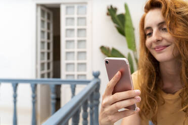 Hand of smiling redheaded young woman holding cell phone, close-up - AFVF03962