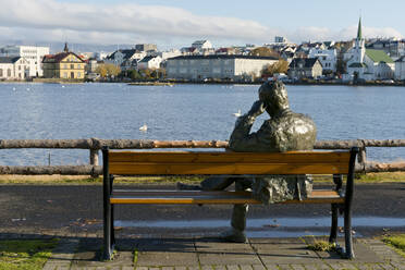 Sculpture of a man sitting on a park bench in front of Tjornin Lake and the Historic Centre of Rykjavik, Iceland, Polar Regions - RHPLF08969