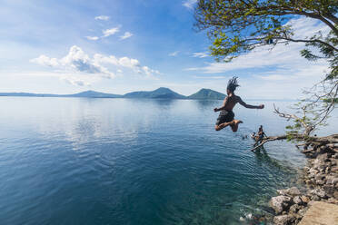 Mann springt in der Bucht von Rabaul mit dem Vulkan Tavurvur im Hintergrund, Ost-Neubritannien, Papua-Neuguinea, Pazifik - RHPLF09145