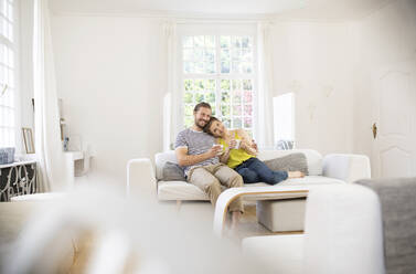 Happy young couple sitting on couch at home - MJFKF00001