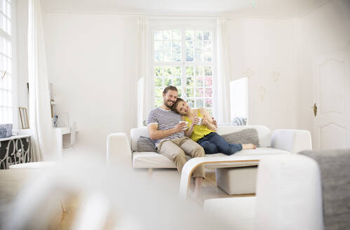 Glückliches junges Paar sitzt zu Hause auf der Couch - MJFKF00001