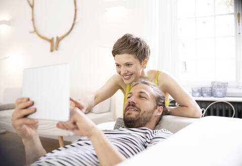 Glückliches junges Paar mit Tablet im Wohnzimmer zu Hause - MJFKF00003