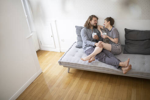 Glückliches junges Paar im Pyjama auf der Couch zu Hause - MJFKF00014