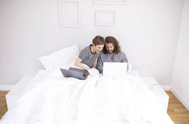 Junges Paar mit Laptops im Bett zu Hause - MJFKF00018