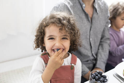 Porträt eines verspielten Jungen mit seiner Familie, der am Tisch Blaubeeren isst, lizenzfreies Stockfoto
