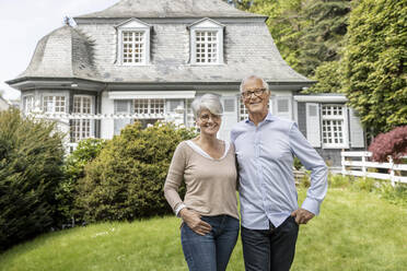 Happy senior couple standing in garden of their home - MJFKF00029