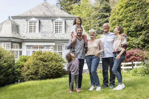 Eine glückliche Großfamilie steht im Garten ihres Hauses, lizenzfreies Stockfoto