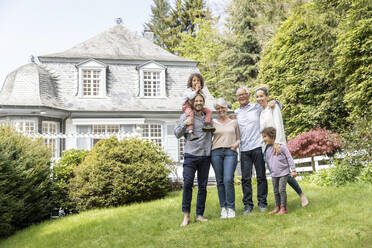 Eine glückliche Großfamilie steht im Garten ihres Hauses - MJFKF00035