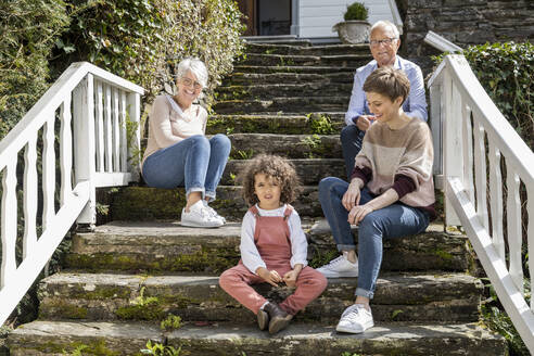 Älteres Ehepaar mit erwachsener Tochter und Enkel auf einer Treppe im Garten ihres Hauses sitzend - MJFKF00038