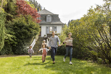 Glückliche Großfamilie beim Laufen im Garten ihres Hauses - MJFKF00040