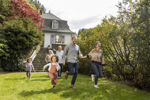 Glückliche Großfamilie beim Laufen im Garten ihres Hauses - MJFKF00041