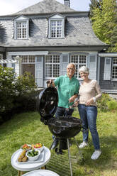 Glückliches älteres Paar beim Grillen im Garten ihres Hauses - MJFKF00044