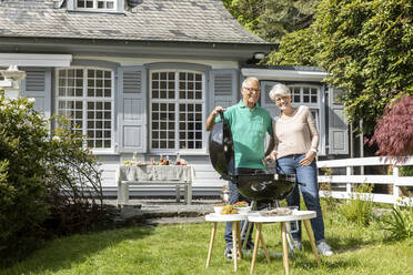 Glückliches älteres Paar beim Grillen im Garten ihres Hauses - MJFKF00045
