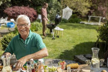 Porträt eines glücklichen älteren Mannes beim Mittagessen im Garten - MJFKF00053