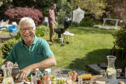 Porträt eines glücklichen älteren Mannes beim Mittagessen im Garten - MJFKF00053